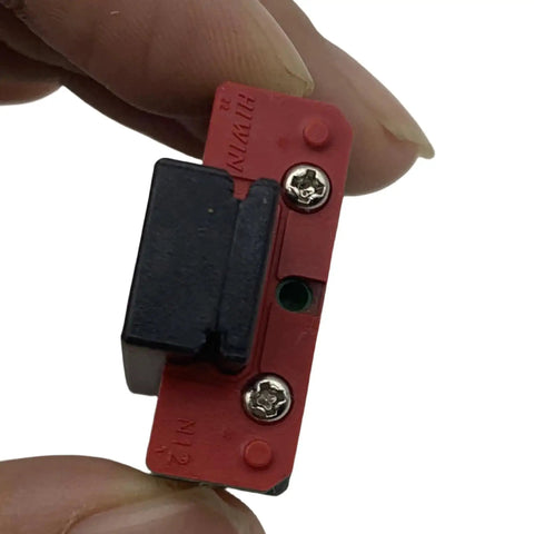 Close-up of a small red and black switch with two screws, being held between fingers, used in electronics or machinery.