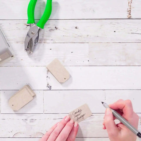Person writing on tags with One Quarter Inch Hole Punch Handheld With Soft Grip Ergonomic Handle for DIY crafts and scrapbooking.