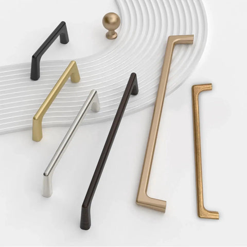 Various cabinet handles in different finishes, including brushed satin nickel, arranged on a textured surface.