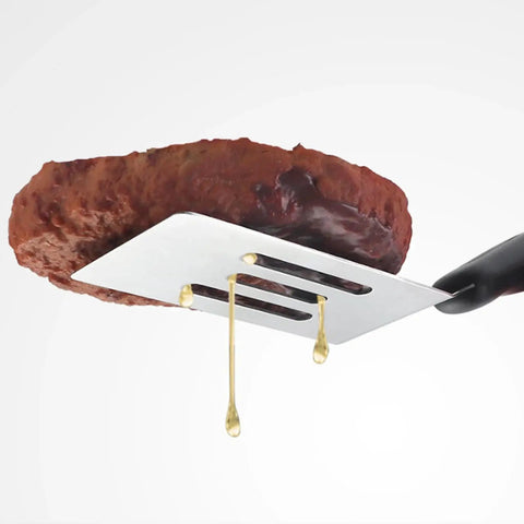 Close-up of metal slotted spatula lifting meat, showing oil drainage. Two Piece Small Metal Spatula Set For Kitchen Use Stainless Steel Slotted And Solid Mini Spatulas.