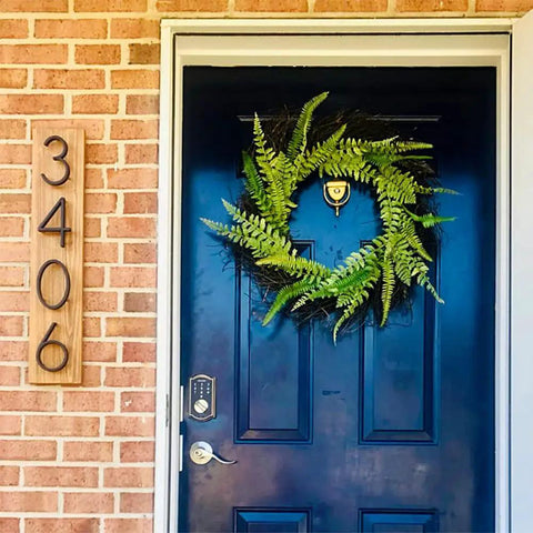 Front view of a house showing a dark blue door with a fern wreath and 3406 displayed on wood, not a 5 Inch Stainless Steel Floating House Number With Nail Kit Coated Black 911 Sign.