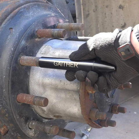 Close-up of a steel vehicle wheel hub with rusted lug studs; gloved hand uses a GAITHER tool.