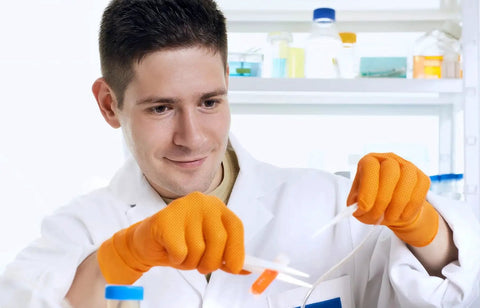 Scientist wearing 8 Mil Orange Nitrile Gloves With Diamond Textured Grip For Industrial And Food handling test tubes in a lab.