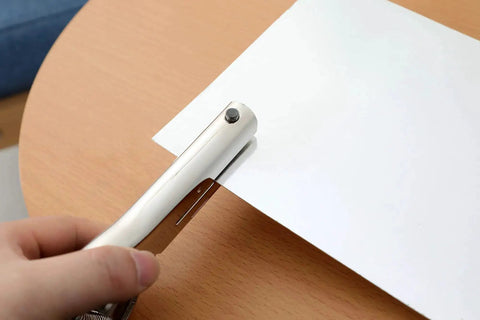 Person using Beefy Heavy Duty 1/8 Inch Single Hole Punch with ultra long depth up to 53mm on a piece of paper on a wooden table.
