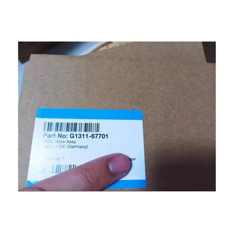 Front view of cardboard box for G1311-67701 electric proportional valve; blue top label with barcode, hand visible.