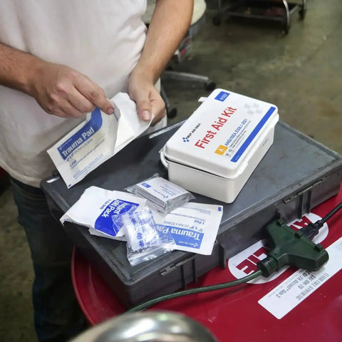 Person using ANSI A 2021 and OSHA compliant 10 person first aid kit with bandages and trauma pads on a worksite table
