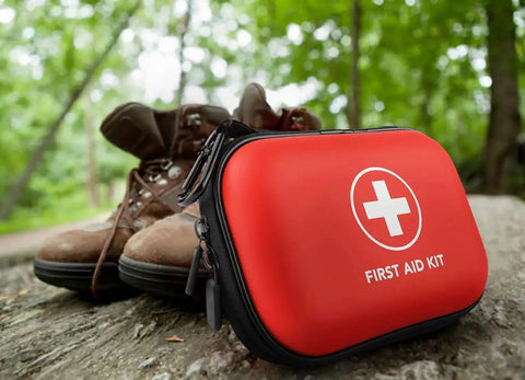 Red Travel Ready 100-Piece First Aid Kit in water-resistant hard shell case on a log with hiking boots, ideal for on-the-go adventures.