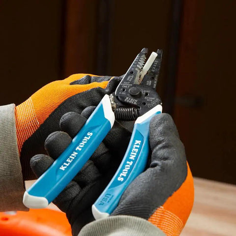 Electrician using Klein Tools wire stripper, wearing protective gloves, in a workshop setting.