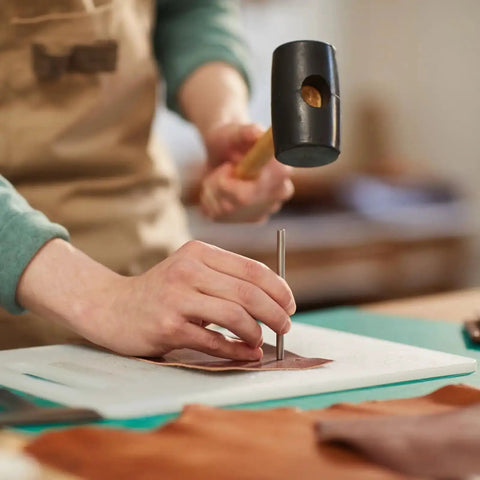 Person using 17 Piece Round Leather Hole Punch Kit 0.5 To 7mm Metal Hollow Punch Tool Set for leather crafting on a workbench.