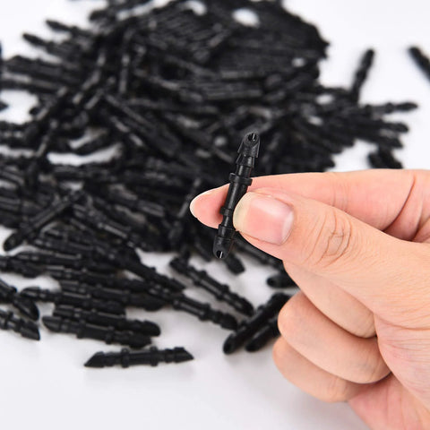 Barbed irrigation connector, 1/4-inch, black plastic, held in hand with many similar fittings in background.