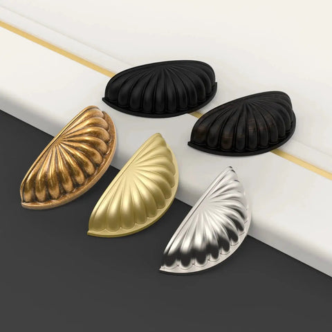 Set of assorted metallic cup pulls on a black and white surface, showing matte black, bronze, gold, and silver finishes for cabinets.