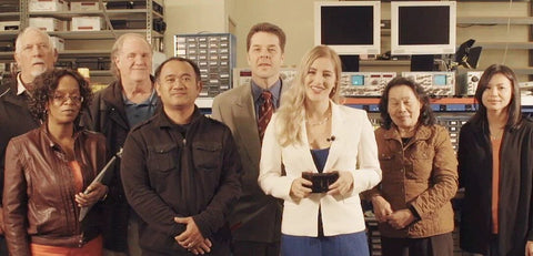 Group of eight people standing in an electronics lab with shelves and equipment in the background.