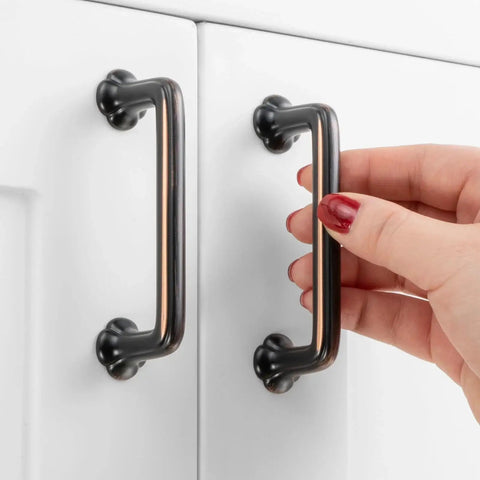 Hand holding 10 Pack 3 Inch Hole Centers Oil Rubbed Bronze Cabinet Pulls with Clover Design, installed on white cabinet