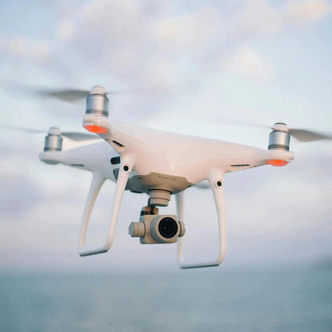 White quadcopter drone flying in the sky with ocean background.
