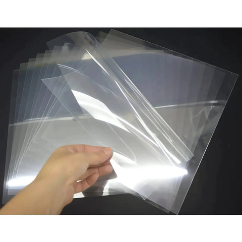 Hand holding a stack of 10 Mil Blank 12x12 Inch Stencil Sheets For Laser Cutting Vinyl And Mylar Projects, Transparent PET Acetate Template Material For DIY Stencils.