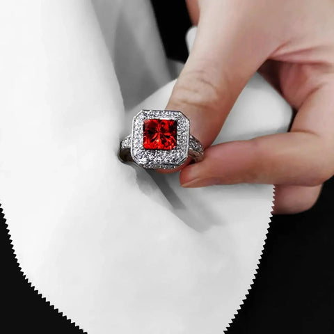 Hand holding a ring with a red gemstone, cleaned with a white microfiber cloth, showcasing 30 Pack Microfiber Cleaning Cloths For Glasses Lenses And Screens 6x7in.