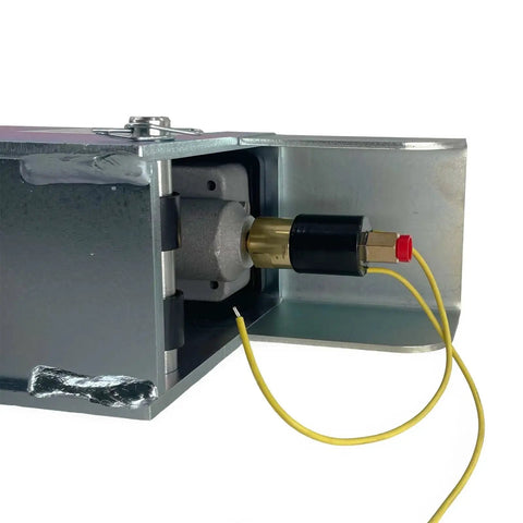 Demco hydraulic surge brake actuator mounted in metal housing; brass piston, black cap, yellow solenoid wires