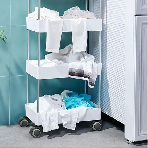 Three-tier laundry cart with white bins filled with clothes against a teal wall near a door.