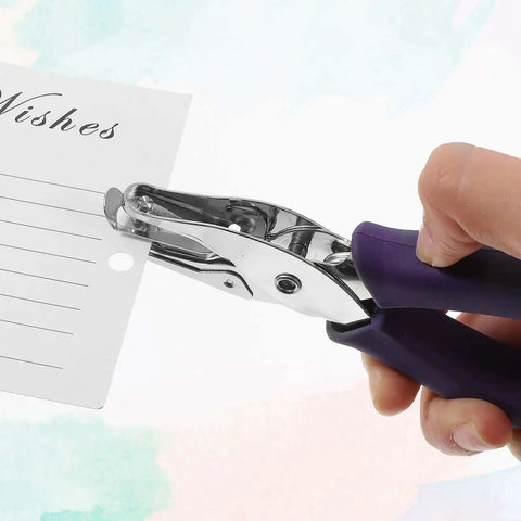 Hand using 16 Pack Handheld Hole Puncher With Soft Grip 1/4 Inch Circle Punch on greeting card, featuring purple grip