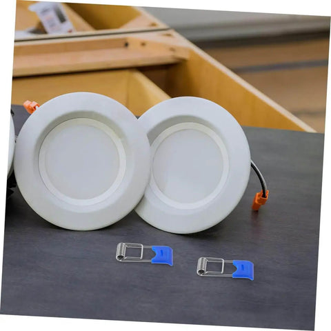 50 Pcs Recessed Light Clips Spring Clips For Downlight Installation next to two white recessed lights on a wooden table