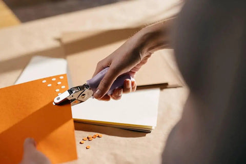 Person using Purple Circle Hand Punch 1/4 Inch for Crafts with Cushioned Grip to punch holes in orange cardstock for scrapbooking.