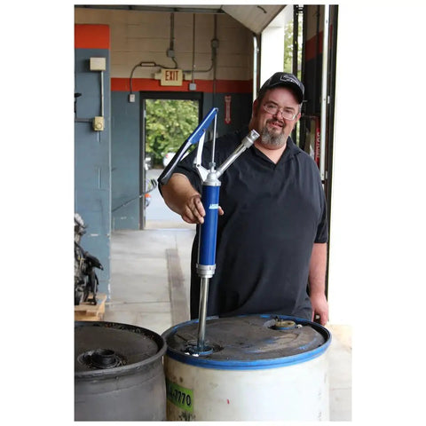Man using Lincoln 1340 Lever Action Barrel Pump for industrial lubrication, attached to a large blue drum in a workshop.