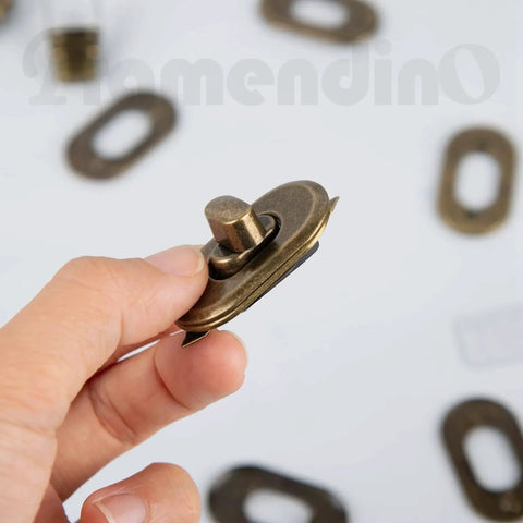 Hand holding an antique bronze twist lock from Twist Lock Clasp Sets For Bags And Leather Projects, 37mm by 21mm.
