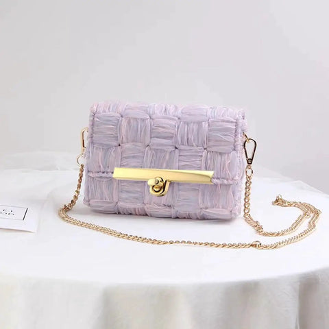 Woven handbag with a gold chain strap and front twist lock clasp placed on a white table.