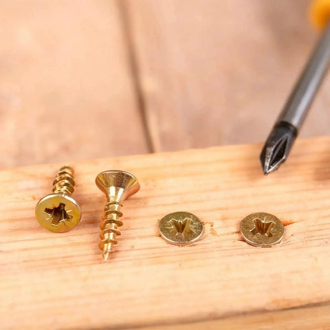 Gold self-tapping flat head screws and Phillips screwdriver on wood, part of the 1170 Pcs Micro Screws Set For Electronics And Eyewear