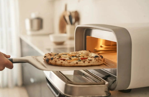 Compact 12 Inch Aluminum Pizza Peel With Handy Handle For Easy Pizza Turning And Oven Prep Lightweight Yet Durable Ideal For Home Kitchens And Ooni Ovens Space Saving Design For Quick Pies being used to remove a pizza from an oven