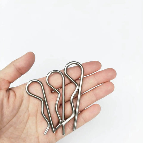 Hand holding three stainless steel cotter pins, part of Six Pack Heavy Duty Cotter Pins M4x85mm Stainless Steel Built Tough For Trailer Hitches And Towing Gear R Clips Hairpin Clips Spring Retaining Wire Pins Rust Resistant Corrosion Proof Ideal For Tractors Mowers Carts And Trucks.