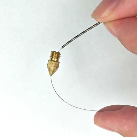 Hand holding a cleaning needle next to a brass 3D printer nozzle from the Complete 42Pcs 3D Printer Nozzle Cleaning Tool Kit.