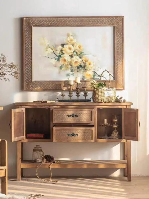 Wooden cabinet with open doors, decorative handles, and a floral painting above; a basket and candles resting on top.