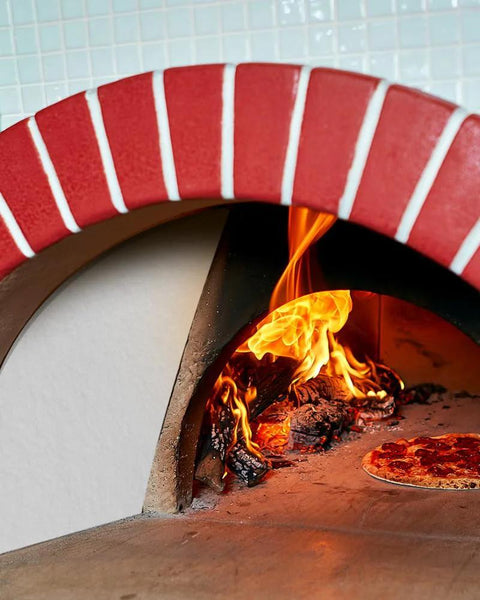 Pizza baking inside a red-brick wood-fired oven with bright orange flames.