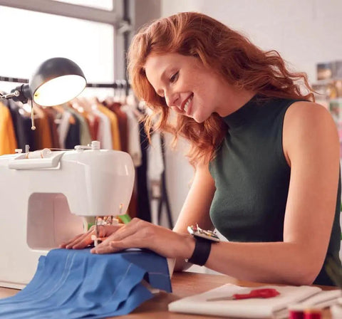 Front view of a white sewing machine stitching blue fabric, worn by a woman in a green sleeveless top.