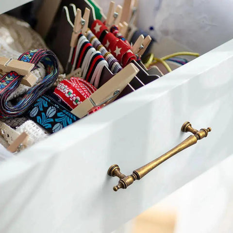 Drawer with Six Pack 5 Inch Antique Brass Cabinet Pulls, showing ornate handles and decorative finials in a vintage setting.