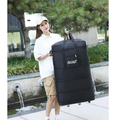 Person carrying Expandable Extra Large Travel Duffel Bag With Six Wheel Spinner in black, made from waterproof Oxford fabric, outdoors.
