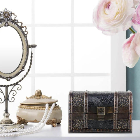 Ornate small wooden jewelry box with metal accents, placed on a vanity next to a pearl necklace and decorative mirror.