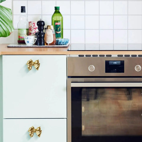 Gold Bow Cabinet Knobs Set Two Pack Brass Finish Bow Shaped Pulls on Kitchen Cabinets Next to Stainless Steel Oven