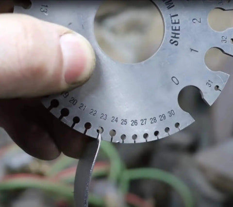 Person using sheet metal gauge to measure thickness in workshop setting, highlighting metal fabrication process.