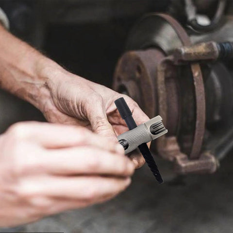 Grease fitting replacement tool with knurled metal body held in hand, used on a rusty vehicle hub