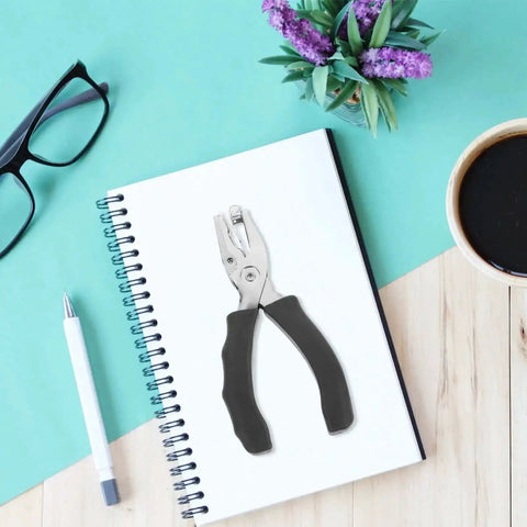 Metal Single Hole Puncher With Ergonomic Handles And Built In Guide on notebook, surrounded by pen and coffee.