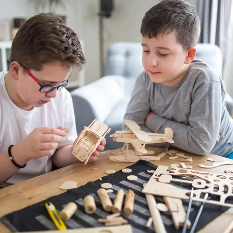 Two kids assembling model airplane from wood kit on table.