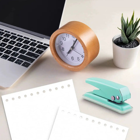 Grab And Go Handheld One Quarter Inch Hole Punch For Up To Twenty Sheets, Metal Hole Puncher With Skid Resistant Base For Paper Chipboard And Art Projects, Green next to a laptop, clock, and plant.
