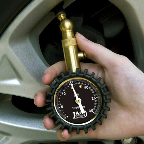 JACO Elite Low Pressure Tire Gauge, brass body with black dial and rubber guard, 0–30 psi, held at tire valve.
