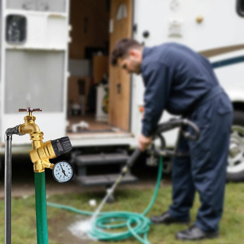 Brass RV water pressure regulator valve with gauge and adjustable knob attached to a green hose by an RV exterior.