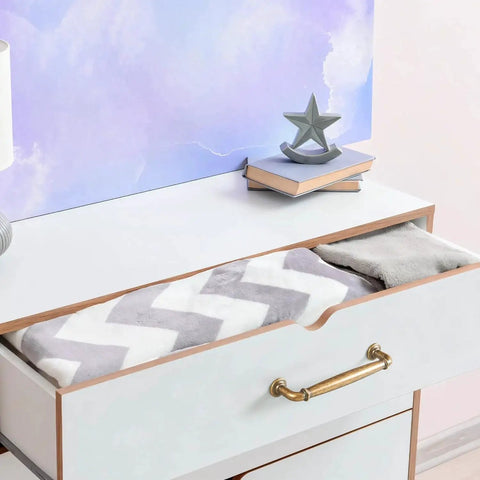 Open drawer with antique brass cabinet handle, featuring chevron-patterned blanket and decorative items on top, showcasing usage.