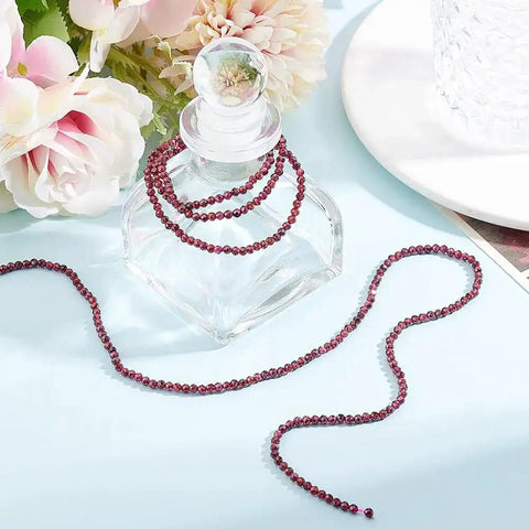 Approximately 270 Pieces 3mm Natural Faceted Garnet Beads For Jewelry Making displayed on a glass bottle with flowers.