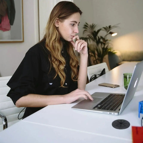 Woman working at desk using laptop with black ABS desk cord hole cover from 4 Pack Desk Grommet Kit With 2 Inch Hole Includes Hole Saw Drill Attachment And 6 Cable Ties For Office And Home Tables