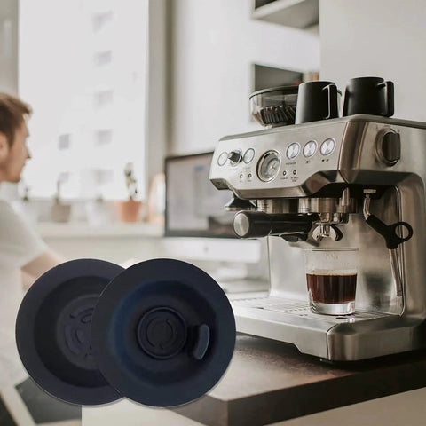 Two blue 54mm espresso backflush cleaning discs, 1 pack, on a kitchen counter beside a stainless espresso machine.